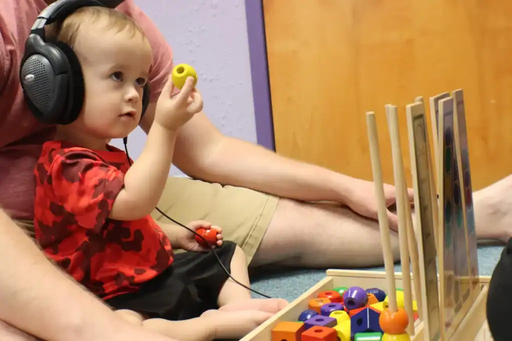 Child engaged in listening therapy combined with finger and hand coordination exercises during a pediatric occupational therapy session.
