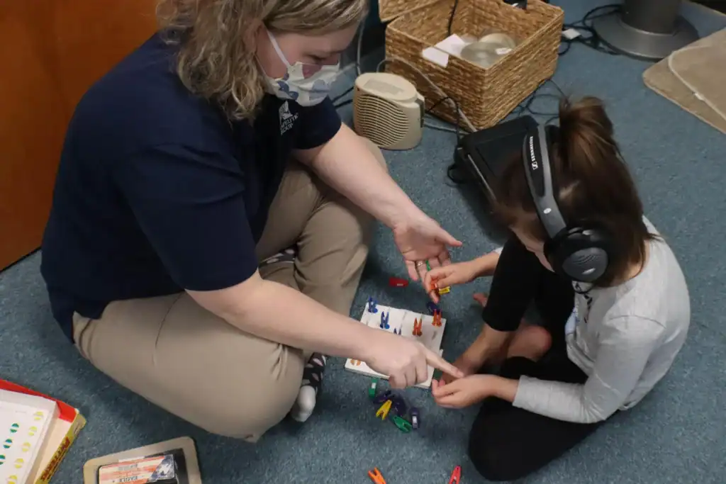 Child engaged in pediatric listening therapy with an occupational therapist to improve sound sensitivity, focus, and bilateral coordination.